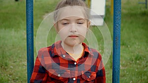 Portrait little girl in red shirt riding on swing. Young happy child with grey eyes on children playard. Inquisitive kid