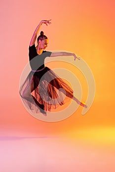 Portrait of little girl, rhythmic gymnastics artist isolated on pink yellow studio background in neon. Concept of sport