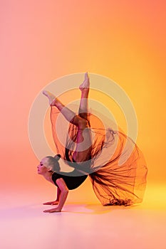 Portrait of little girl, rhythmic gymnastics artist isolated on pink yellow studio background in neon. Concept of sport