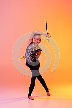 Portrait of little girl, rhythmic gymnastics artist  on pink yellow studio background in neon. Concept of sport