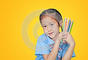 Portrait little girl in school uniform holding color pencils over yellow background. Education and school concept