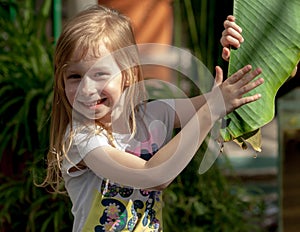 Portrait, little girl of seven years, holds large leaf of palm tree