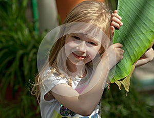 Portrait, little girl of seven years, holds large leaf of palm tree