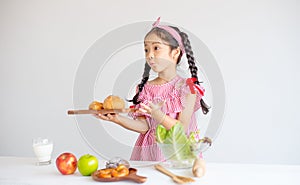 Portrait of little girl show action of surprise and hold plate with bread in front of white wall background
