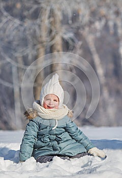 Portrait of little girl sit in snowdrift in winter forest