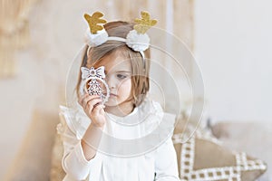Portrait of a little girl Toddler with a headband on her head in the form of deer horns and a Christmas toy in her hands.