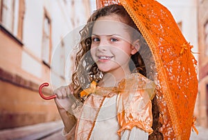 Portrait of little girl wearing a beautiful colonial costume and holding an orange umbrella in a blurred background