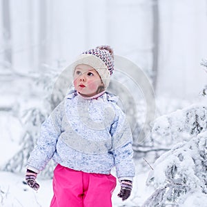 portrait of a little girl in winter hat in snow forest at snowflakes background