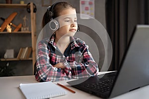 Portrait of little girl in wireless headset using laptop, studying online at home, interested happy student, e-learning