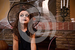 Portrait of a little girl in witch costume and wizard hat against a cobweb-covered fireplace. Halloween festival concept