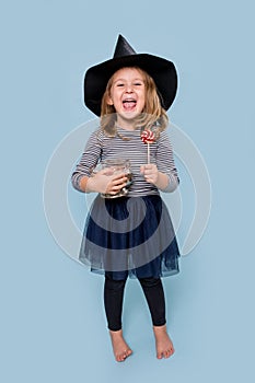 Portrait of a little girl in witch hat holding lollipop and jar full of treats