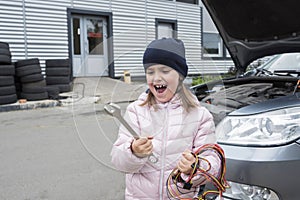 Portrait of a little girl with a wrench, on a background of a car. Auto repair concept