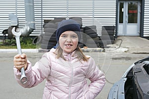 Portrait of a little girl with a wrench on the background of a car service.  Childrens auto mechanic. Automobile Repair Service