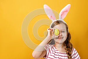 Portrait of a little girl on a yellow background with an Easter egg. Happy cheerful child in the ears of a bunny