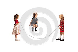 Portrait of little girls, children playing together, jumping over a rope isolated on white studio background