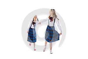 Portrait of little girls, twins having fun together, posing isolated over white studio background. Nice walk