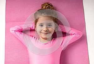 Portrait of a little gymnast girl with her hands under her head lying down on the yoga mat after the exercises.