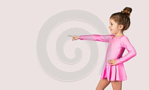 Portrait of a little gymnast girl in pink dress pointing with index finger to one side picture for advertising banners