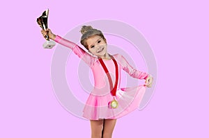 Portrait of a little gymnast girl right after winning dressed in a pink dress with a gold medal around her neck, Holding