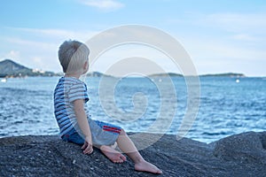 Portrait of little handsome boy sitting on rock near sea water, Thailand