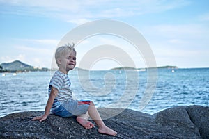 Portrait of little handsome boy sitting on rock near sea water, Thailand