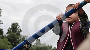 Portrait of little happy child holding blue wooden oar on lake in park. Little adorable kid rows boat. Close up view. Happy little