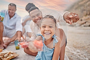 Portrait of a little hispanic girl having a snack while on a picnic with her family at the beach. Mixed race girl having