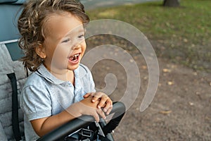 Portrait of a little joyful and laughing child sitting in a baby carriage outdoors