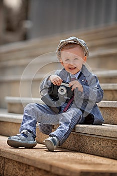 Portrait of a little kid boy photographer taking picture with retro vintage photo camera on the steps outside