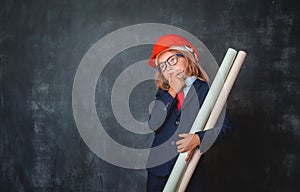 Portrait of little kid in safety helmet and suit thinking about aspirations. Little businessman in glasses looking up