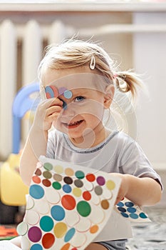 Portrait of a little lovely girl. Cute toddler sticks stickers on herself. Lovely blonde baby in a blue t-shirt.