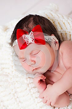 Portrait of little newborn baby girl with a red bow on her head. Sleeping kid.