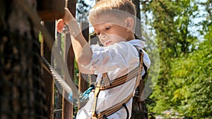 Portrait of little oy holding tight the rope while climing over obstacles in adventure park