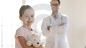 Portrait of little patient with pleasant male doctor on background.