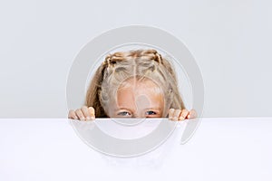 Portrait of little preschool girl, child playing hide-and-seek game isolated over white studio background.