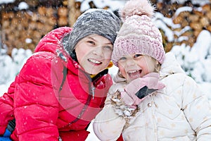Portrait of little preschool girl and school boy playing with snow in winter. Brother and cute sister together during