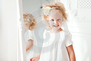 Portrait Little pretty smiling girl in white dress playing in white room