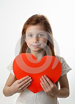 Portrait of little red haired girl with big red heart in her hands