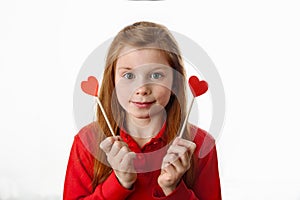 Portrait of little red haired girl with red hearts on sticks in her hands