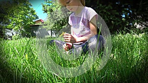 Portrait of a little sad girl sits on the lawn under the spruce