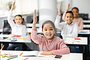 Portrait of little school children raising hands at classroom