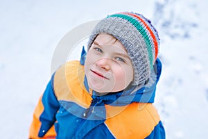 Portrait of little school kid boy in colorful clothes playing outdoors during snowfall. Active leisure with children in