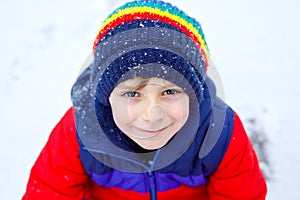 Portrait of little school kid boy in colorful clothes playing outdoors during snowfall. Active leisure with children in