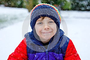 Portrait of little school kid boy in colorful clothes playing outdoors during snowfall. Active leisure with children in