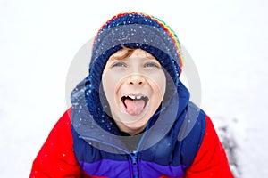 Portrait of little school kid boy in colorful clothes playing outdoors during snowfall. Active leisure with children in