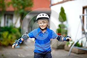 Portrait of little school kid boy in safety protection clothes scating with rollers. Active sporty child doing sports on