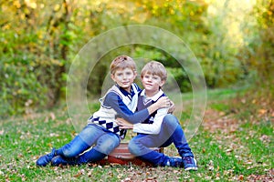 Portrait of little school kids boys sitting in forest. Happy children, best friends and siblings having fun on warm