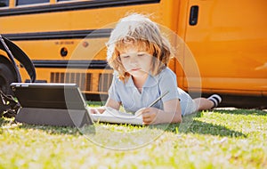 Portrait of little schoolboy writing outdoor in schoolyard park and doing homework.
