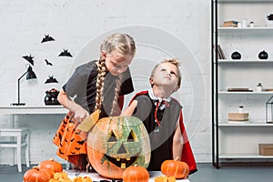 portrait of little siblings in halloween costumes near table with pumpkins