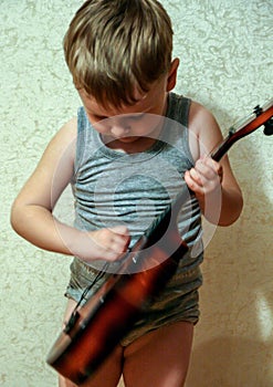 Portrait of a little smiling blond boy playing guitar, blur and grain effect.Funny children.